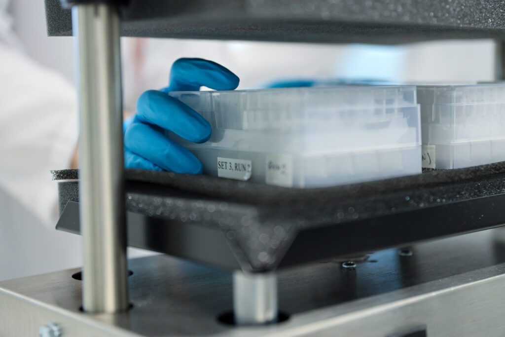 Close up of a gloved scientist hand removing a test tube rack from a shelf of test tube racks.